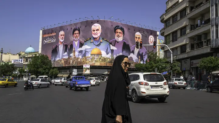 People move past a large banner featuring portraits of slain leaders from Iran-aligned armed groups, including Hamas leader Yahya Sinwar, Hezbollah leader Hassan Nasrallah, and Iranian commander Qasem Soleimani, in central Tehran, Iran, on May 1, 2025. (MOHAMMADALI NAJIB/Middle East Images/AFP via Getty Images)