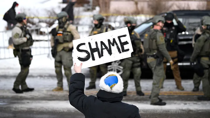 An onlooker holds a sign that says "Shame" as law enforcement officers investigate a shooting by an ICE agent during federal operations in Minneapolis Wednesday. (Stephen Maturen/Getty Images)