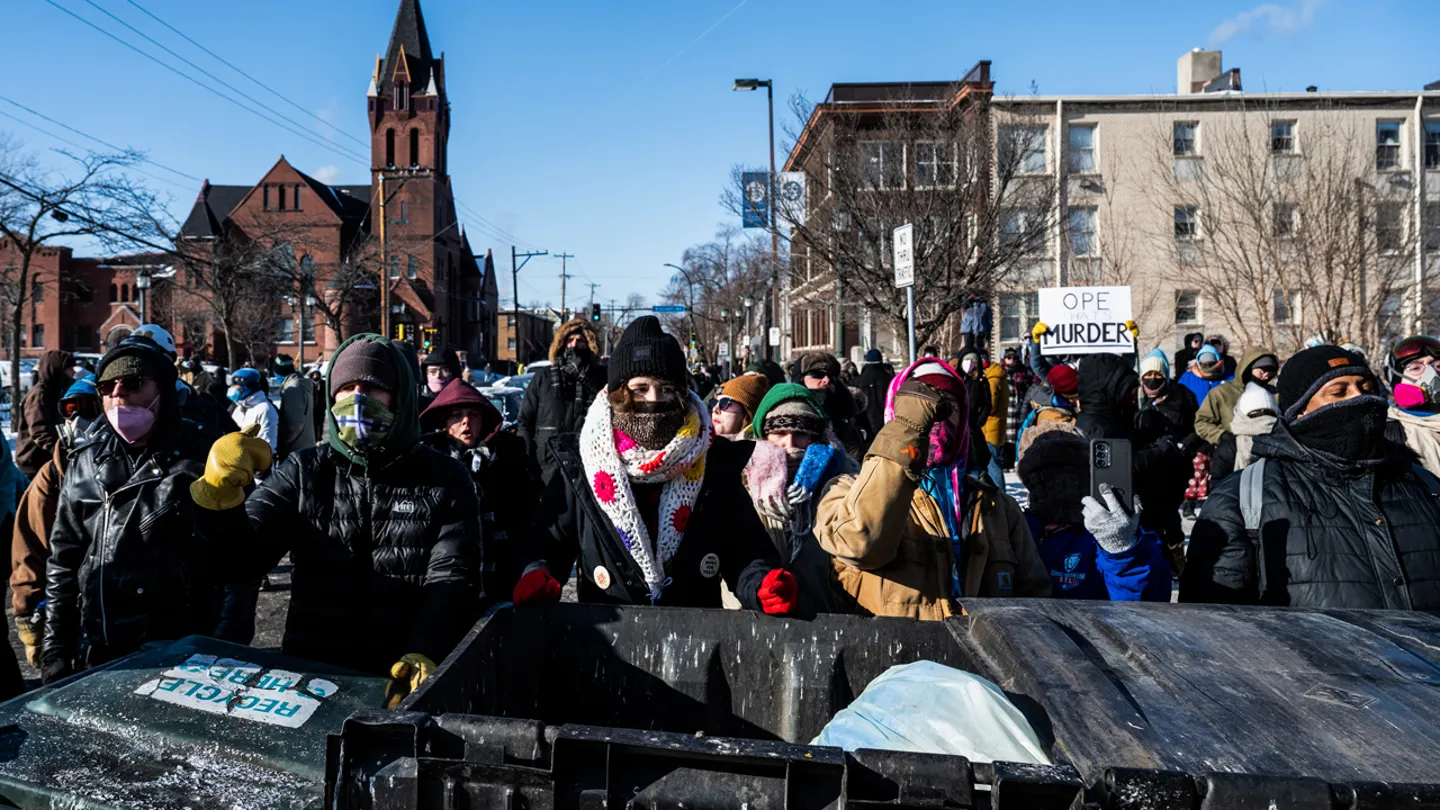 Demonstrators stand behind a barricade of trash bins as they gather near the site where state and local authorities say a man was shot and killed by federal agents earlier in the morning in Minneapolis Jan. 24, 2026. (Roberto Schmidt/AFP via Getty Images)