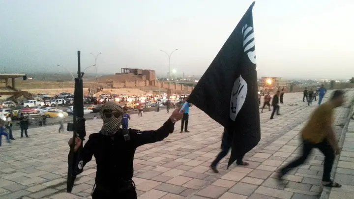 A fighter of the Islamic State of Iraq and the Levant (ISIL) holds an ISIL flag and a weapon on a street in the city of Mosul, June 23, 2014. (Reuters Photo)