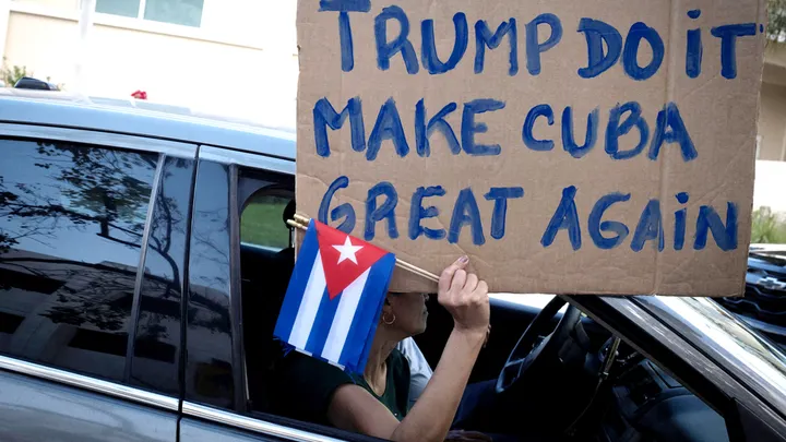 A woman holds a sign and Cuban flags as supporters of U.S. President Donald Trump participate in a protest against Cuba's government in Miami Feb. 28, 2026.  (Marco Bello/Reuters)