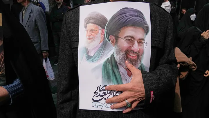 A mourner holds a poster depicting Ayatollah Mojtaba Khamenei, right, the successor to his late father, Ayatollah Ali Khamenei, left, as supreme leader, during the funeral procession for senior Iranian military officials and civilians killed during the campaign in Tehran, Iran, March 11, 2026. (Vahid Salemi/The Associated Press )